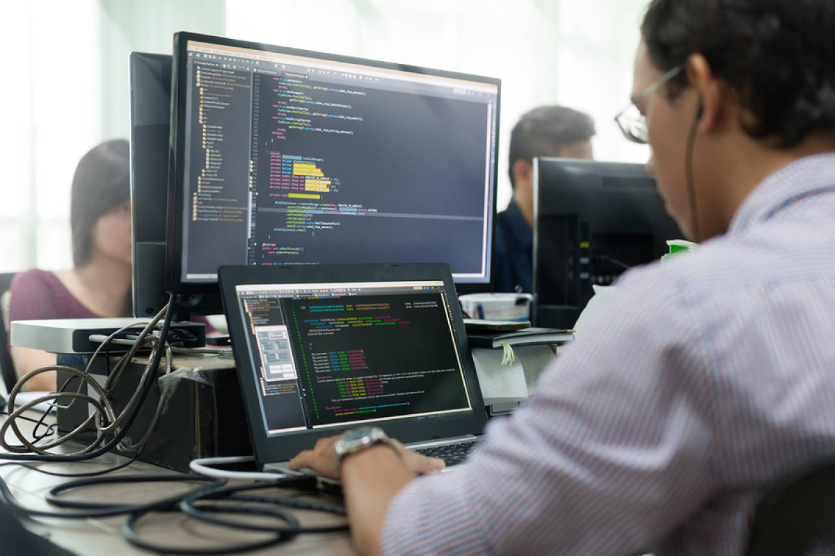 A photo of a programmer sitting in front of his computer, writing lines of code.