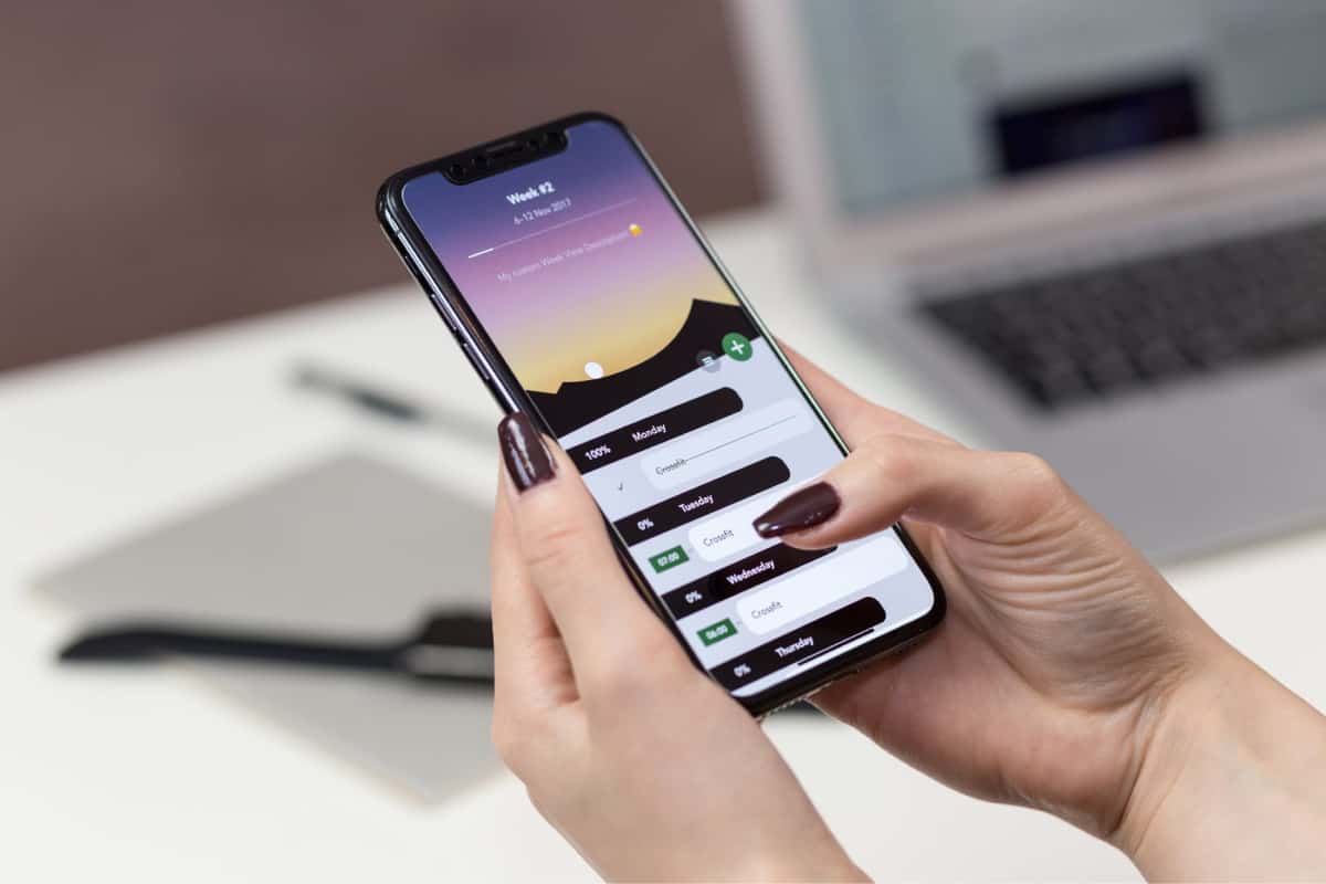 A photo of a woman with painted nails holding a smartphone with an app on the screen.