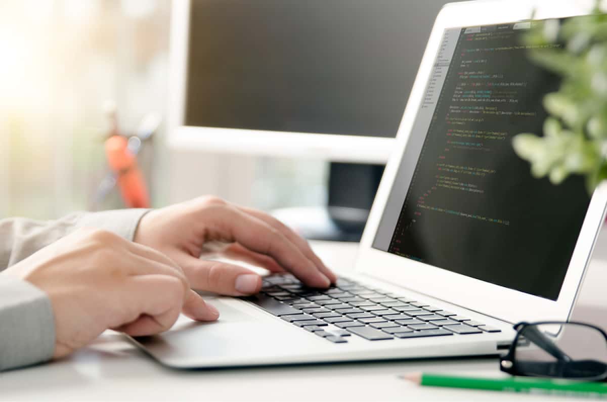 A photo of a person sitting at their desk with a laptop open, displaying lines of code.