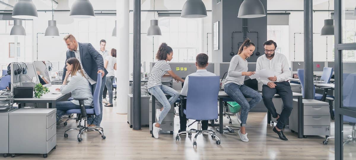 A photo of an open-layout office, with multiple employees, huddled together, working together on various projects.