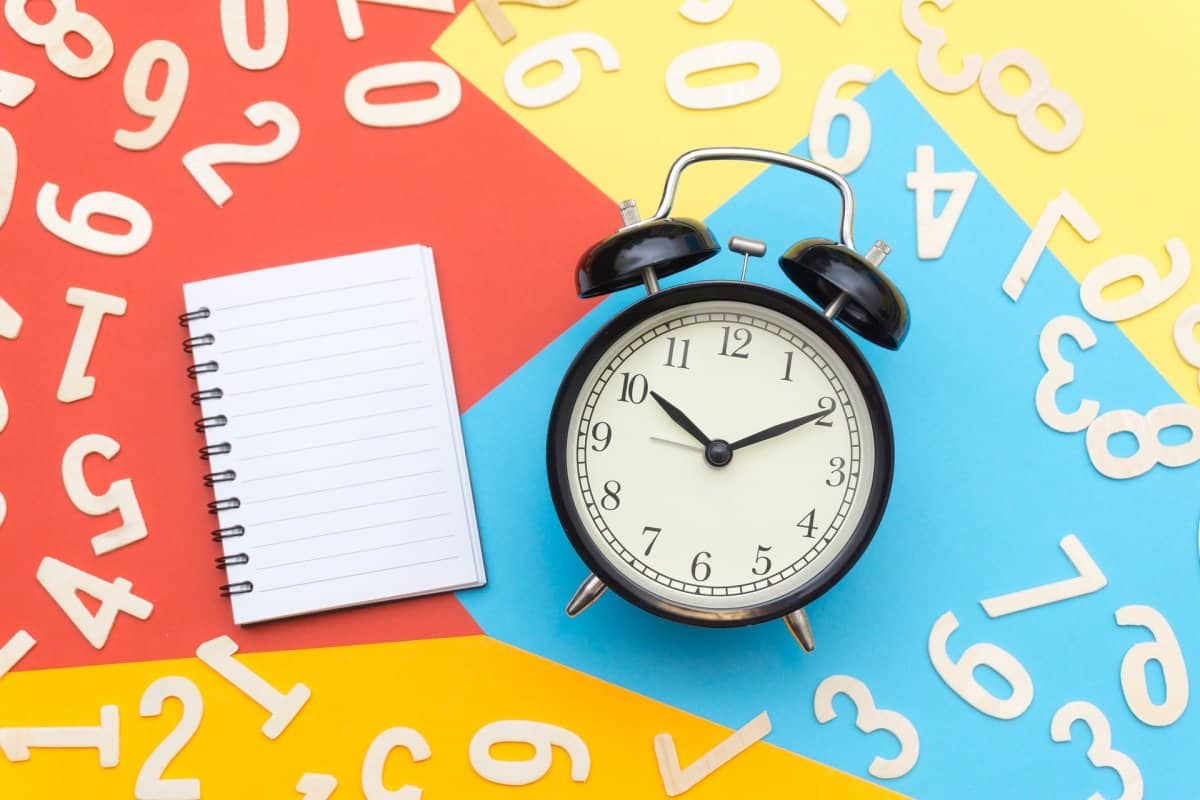 A clock and notebook surrounded by numbers on a two-tone background.