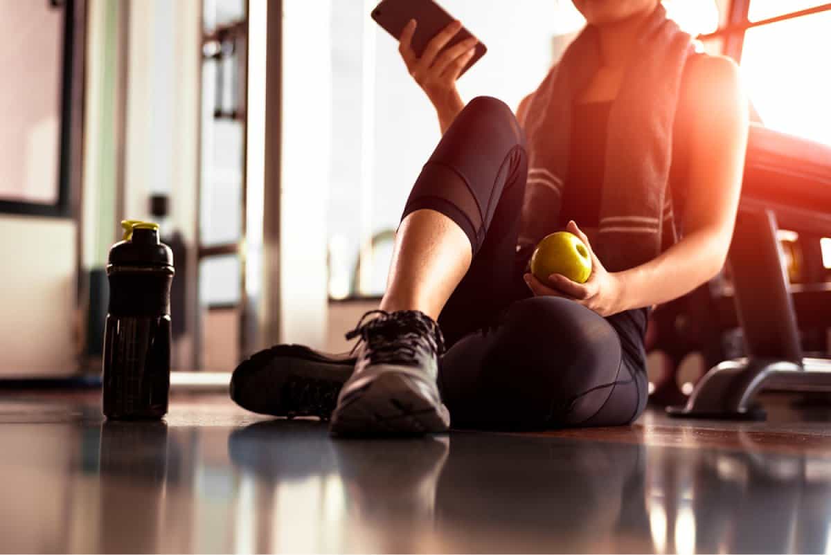 A photo of a woman sitting on the floor, eating an apple after her workout.