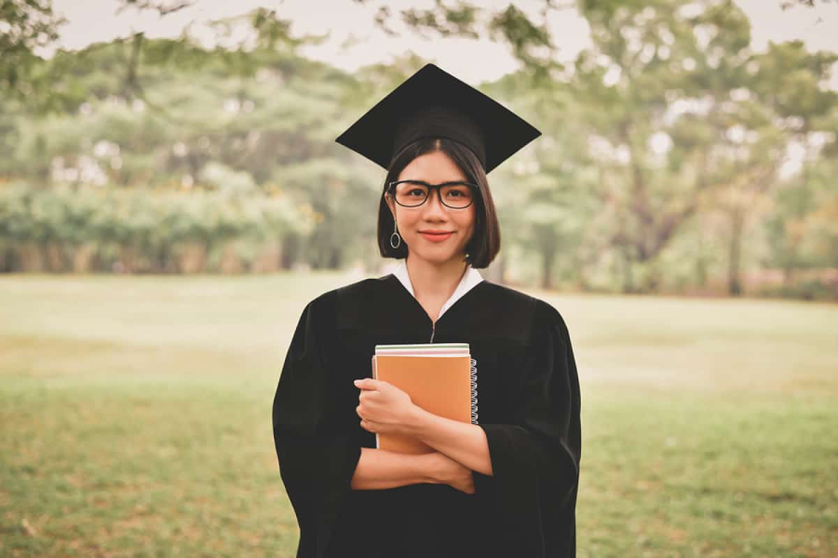 A photo of a happy graduate holding a notebook to her chest.