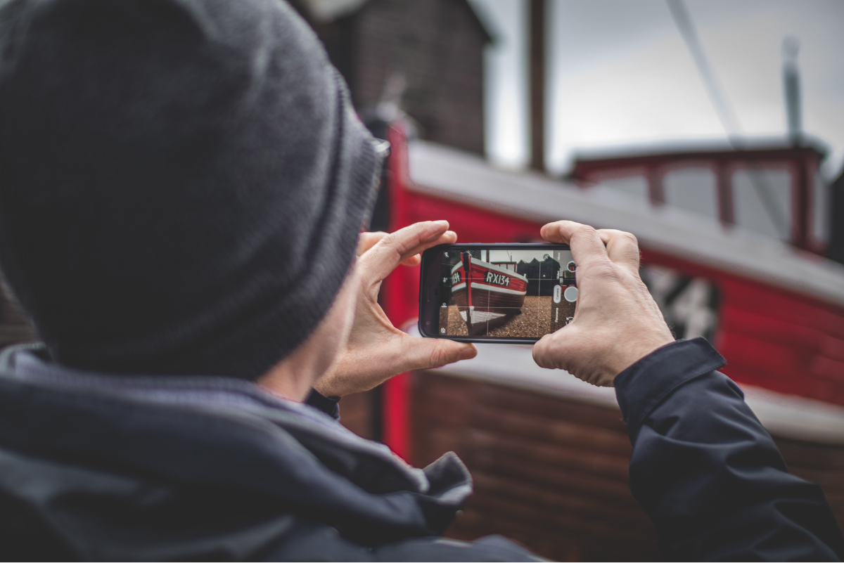 A photo of a person taking a picture of a boat with his smartphone.