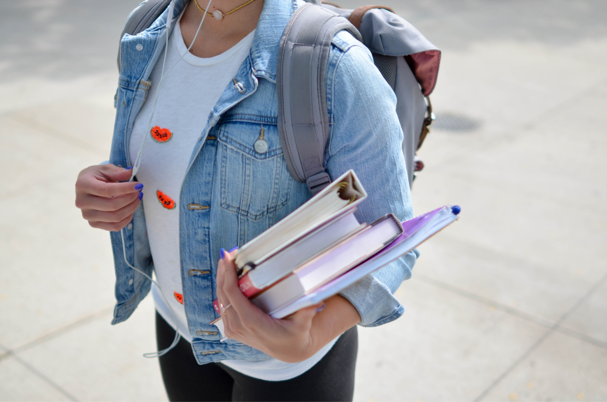 A photo of a college student carrying a stack of notebooks and books on her way to class. 