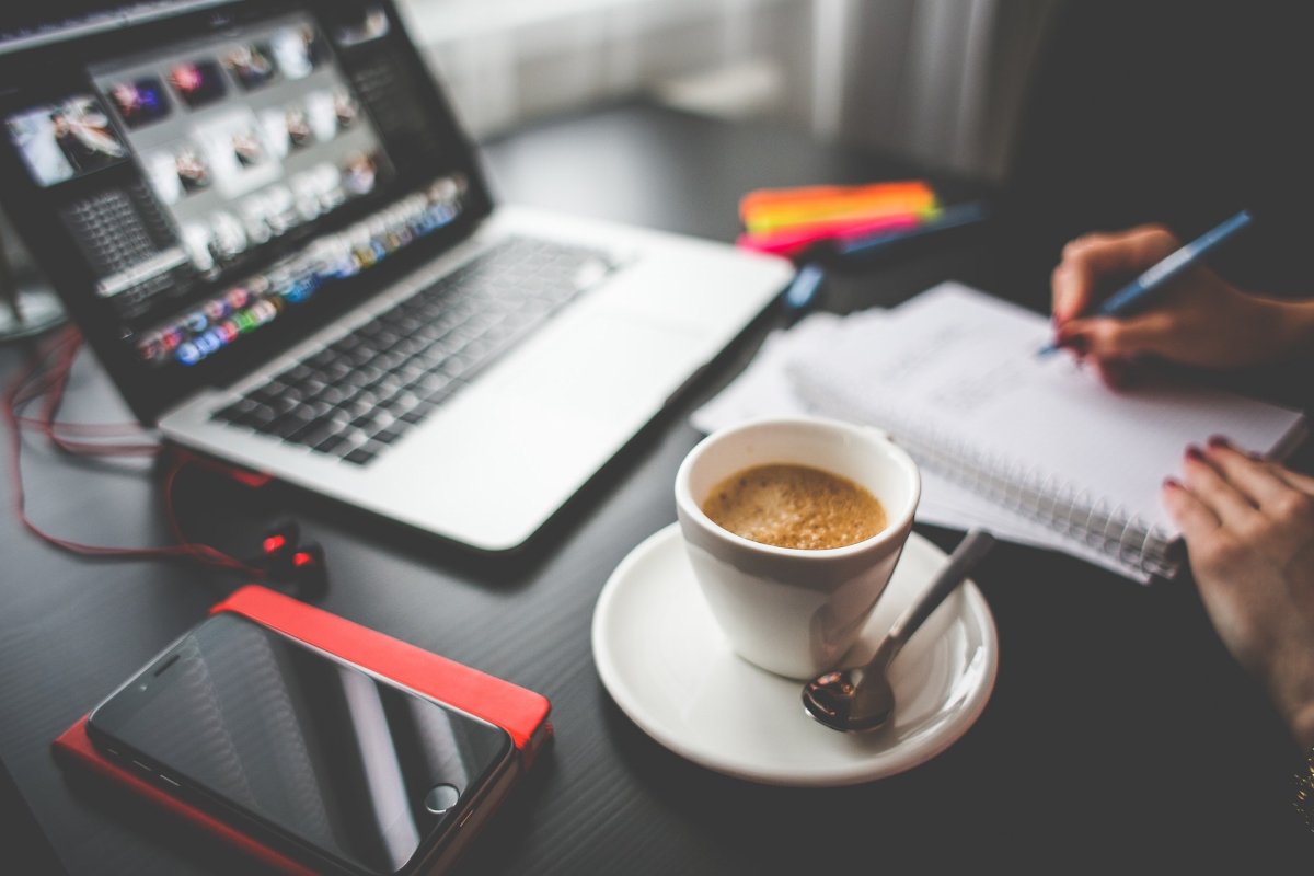 A person working at their desk with their laptop, notebook, and coffee.