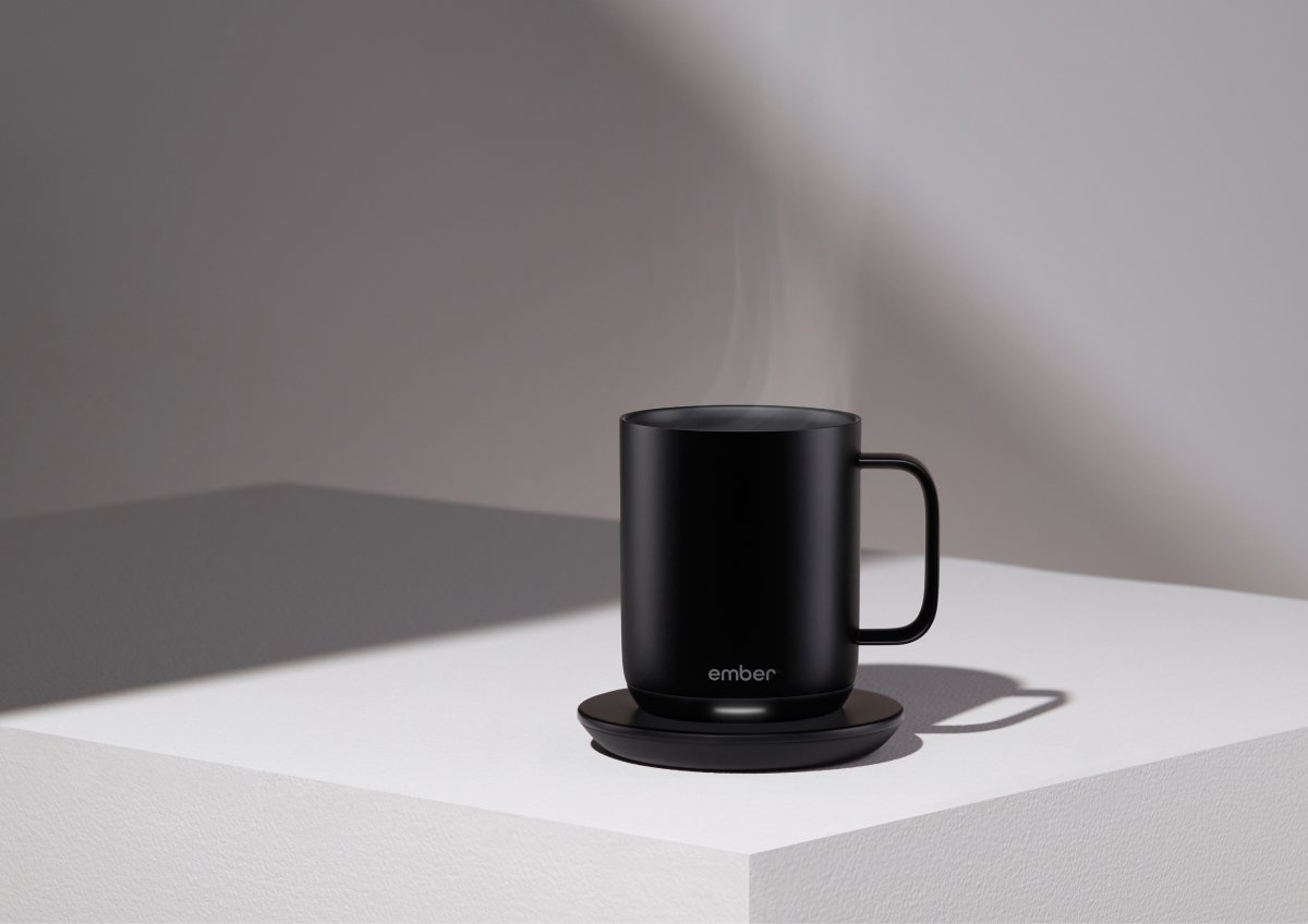 A photo of an Ember mug full of piping hot coffee sitting on a charging coaster. 