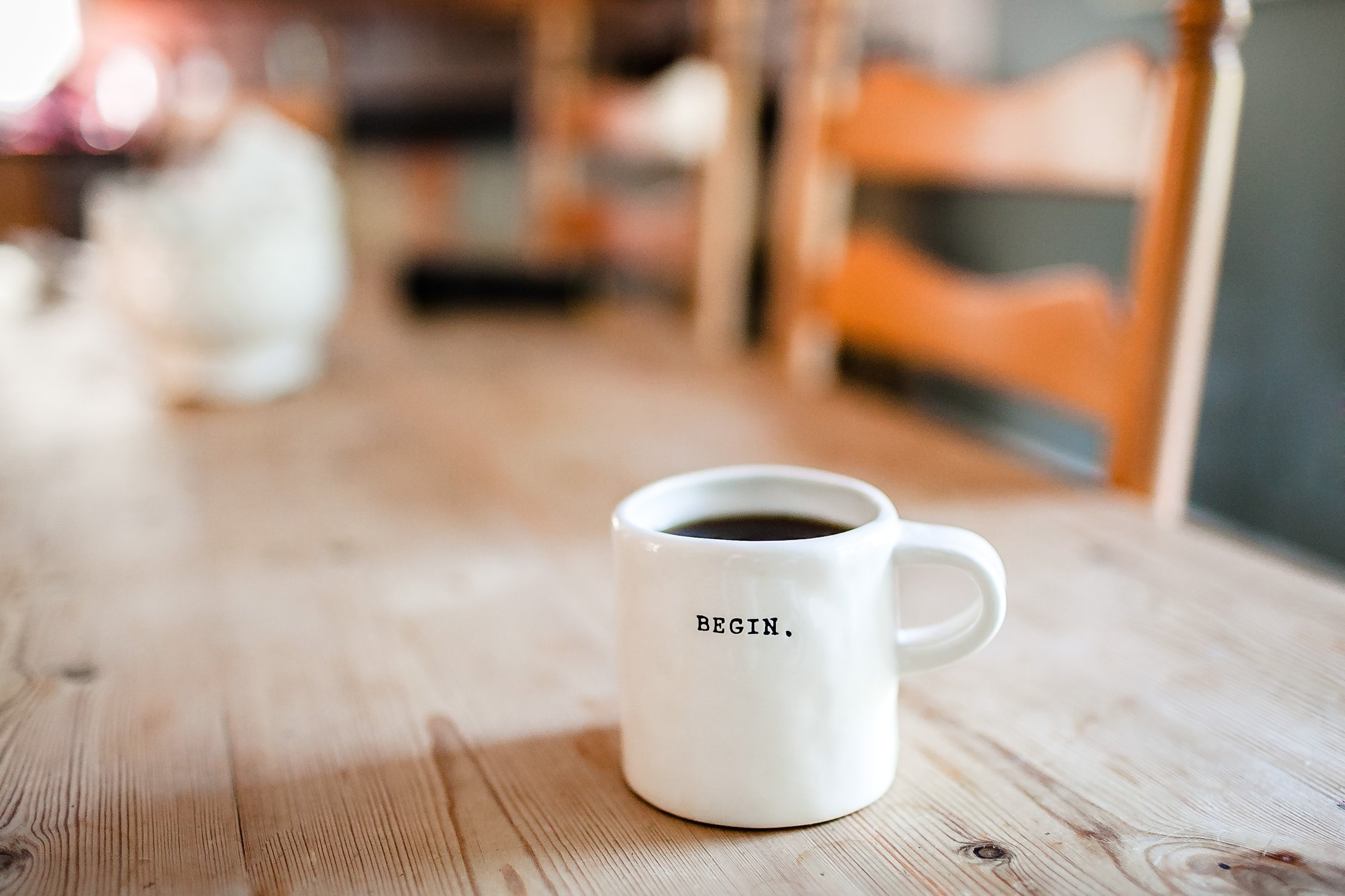 A photo of a white mug filled with coffee with the word “BEGIN” in black typewriter font printed on it.