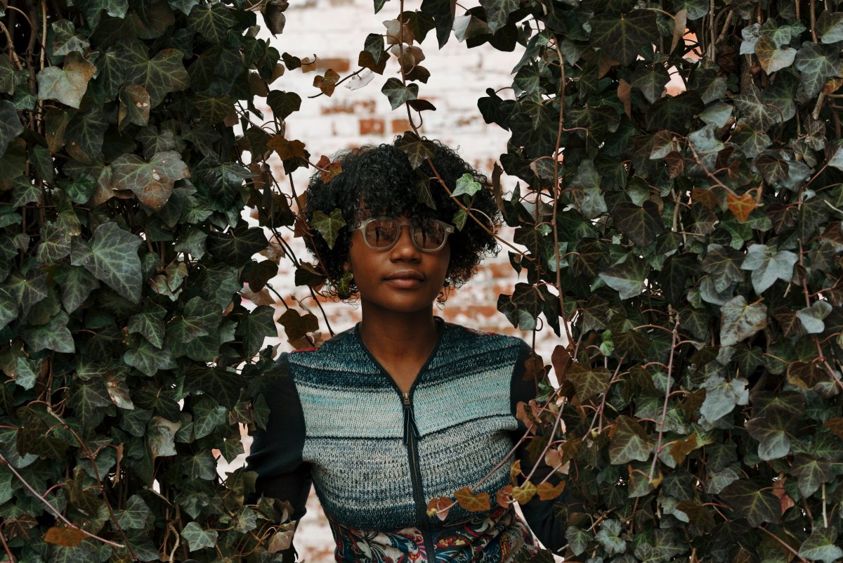 A photo of a woman standing among towers of ivy wearing Genusee sunglasses.