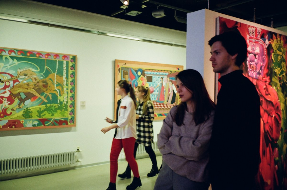 Two people looking at a painting in a busy art museum.