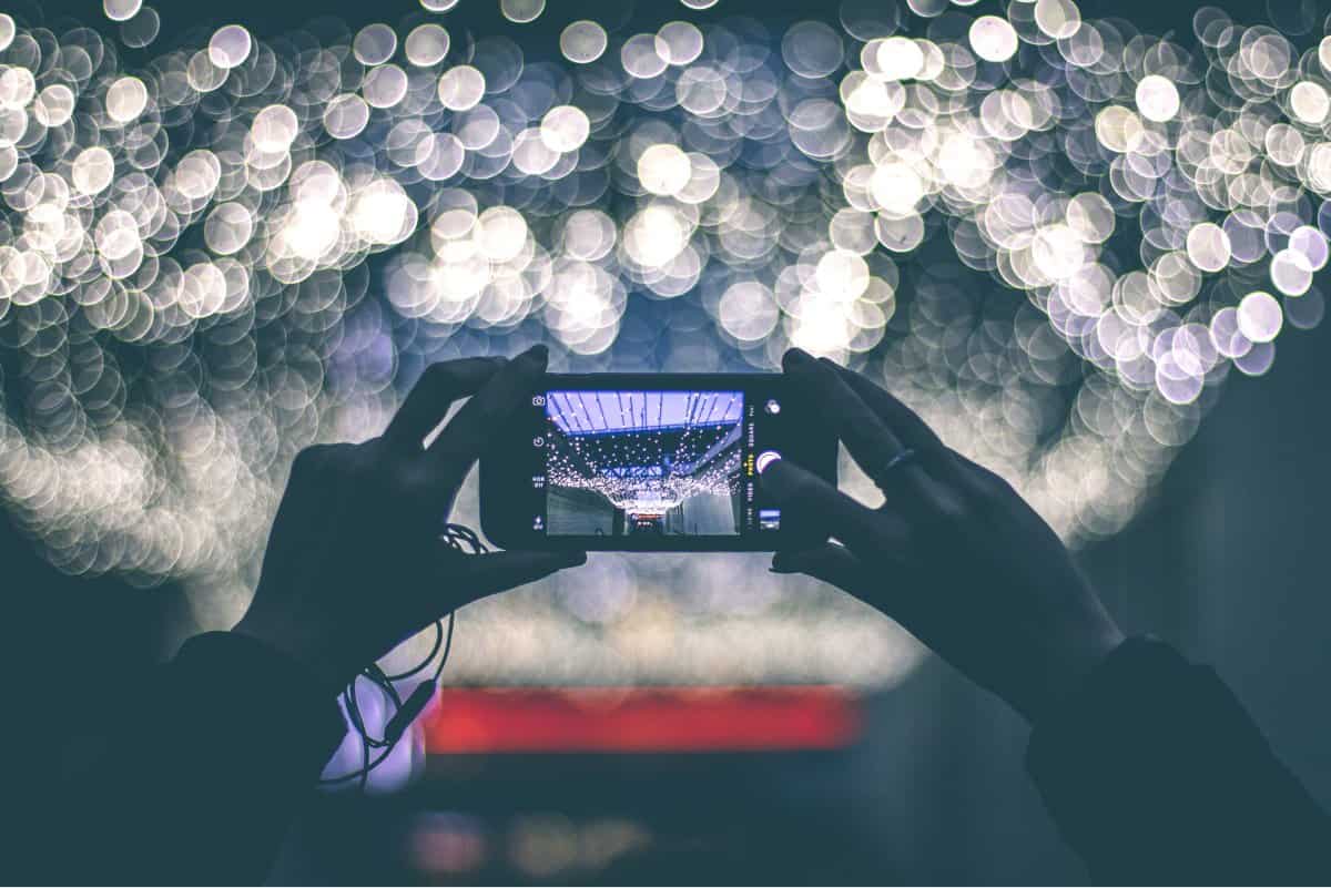 A photo of someone holding up a smartphone to take a picture of light strands draping a ceiling.