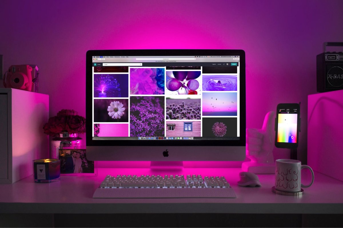 An iMac and iphone on a well designed desk covered in pink light. 