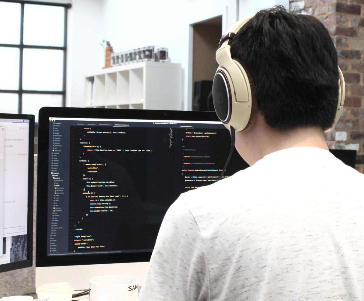 A photo of a mobile app developer wearing headphones while he works on his computer.