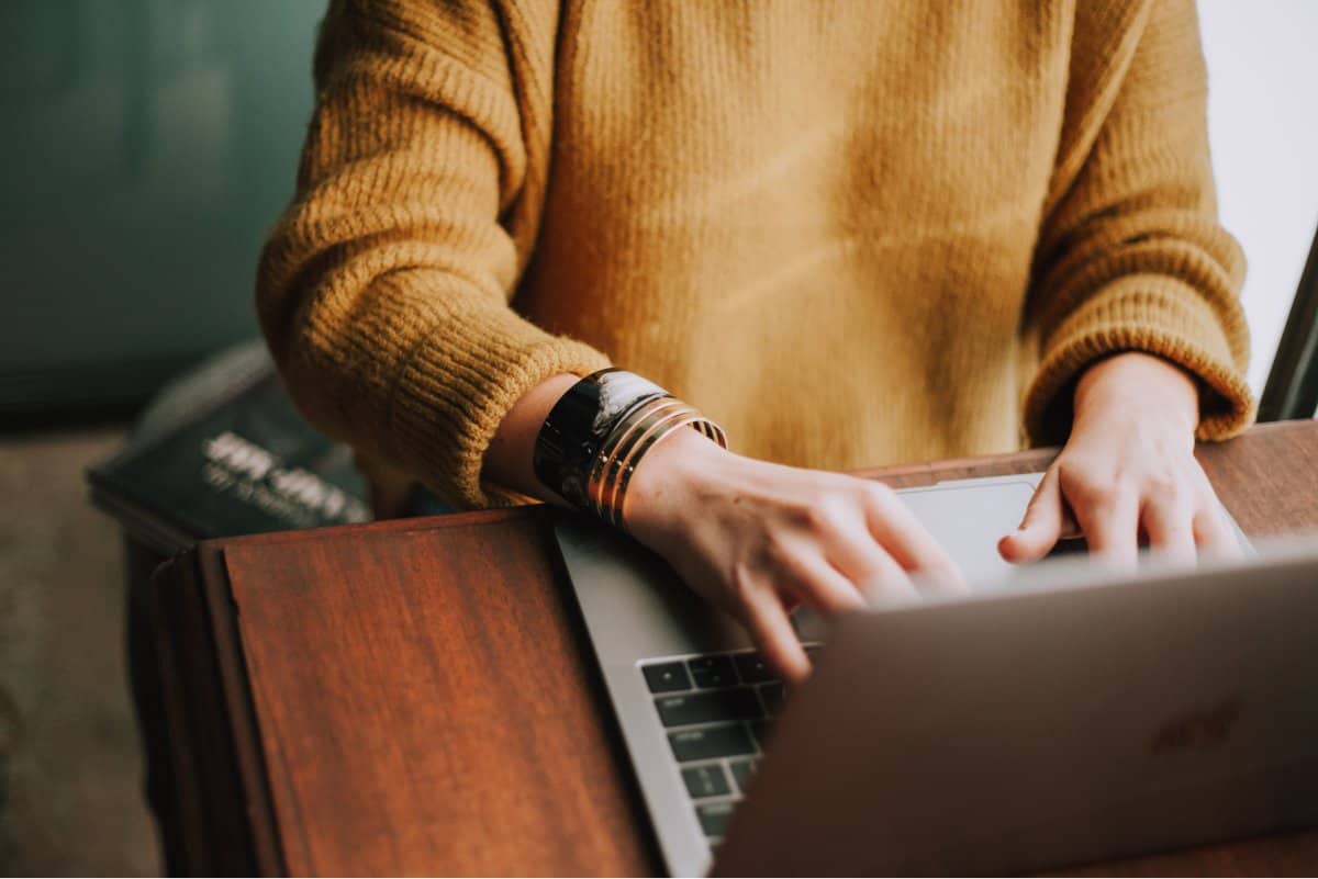 A photo of a woman sitting at a desk and typing on a laptop.