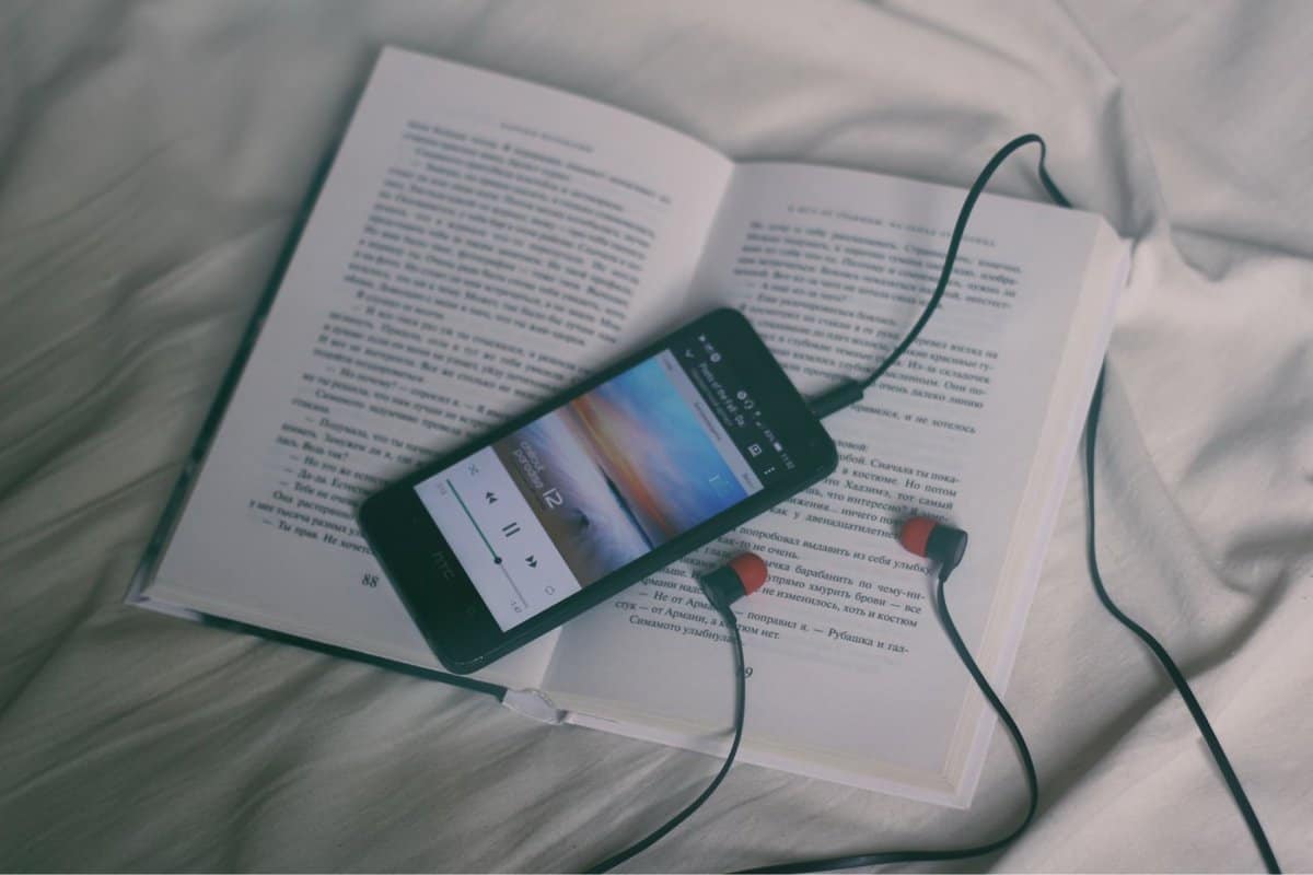 A photo of a smartphone and a set of earbuds resting on an open book.