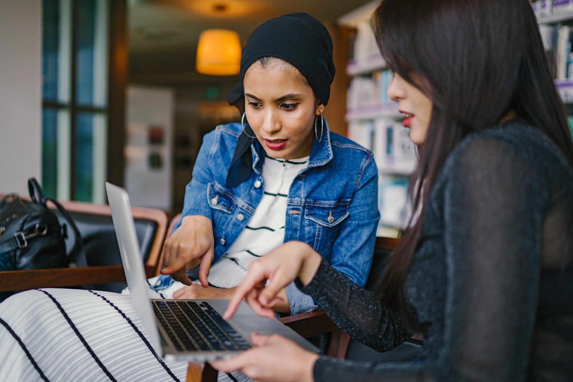 Two women meeting and pointing at a computer screen. 