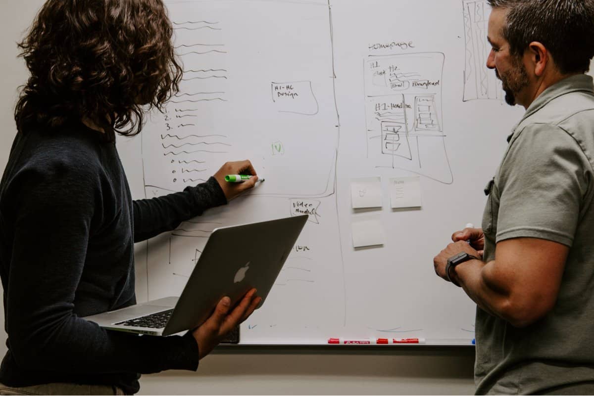 A photo of two members of a mobile app design team thinking through problems by sketching on a dry erase board.