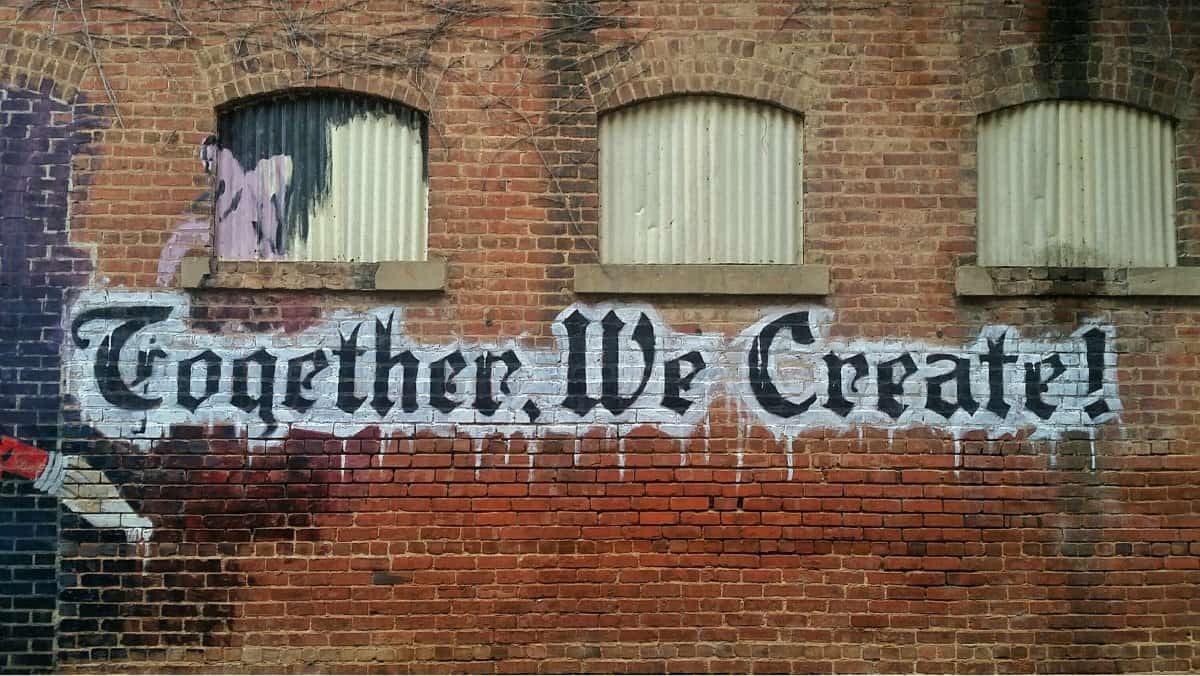  A photo of a graffiti sign on a brick building that says “Together, We Create!”