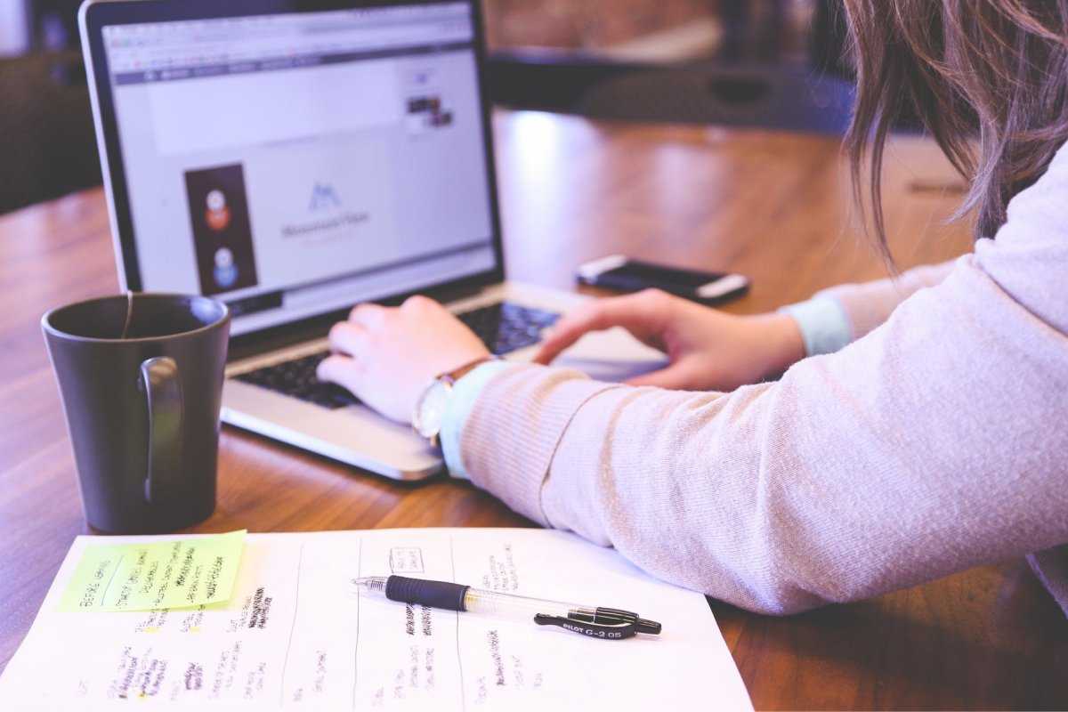  A person working at their laptop with notes, a mug, and their smartphone closeby. 