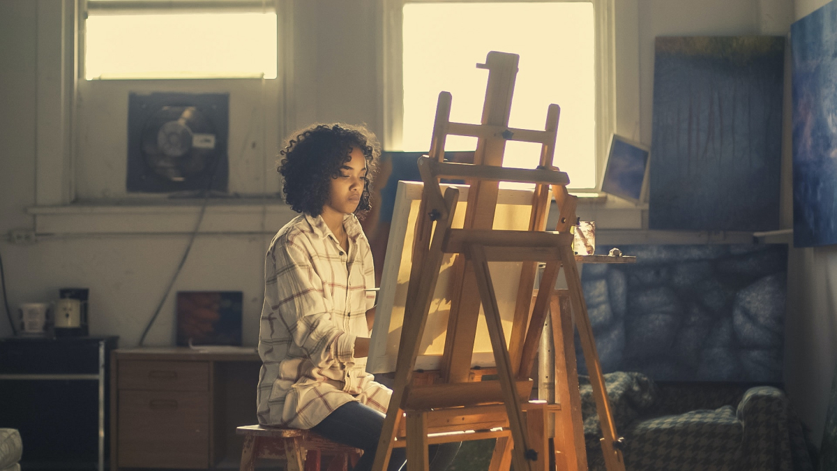 A woman focusing on her painting bathed in warm light. 