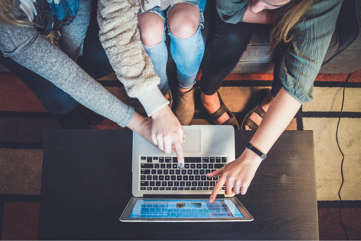 A bunch of women pointing at a laptop screen.