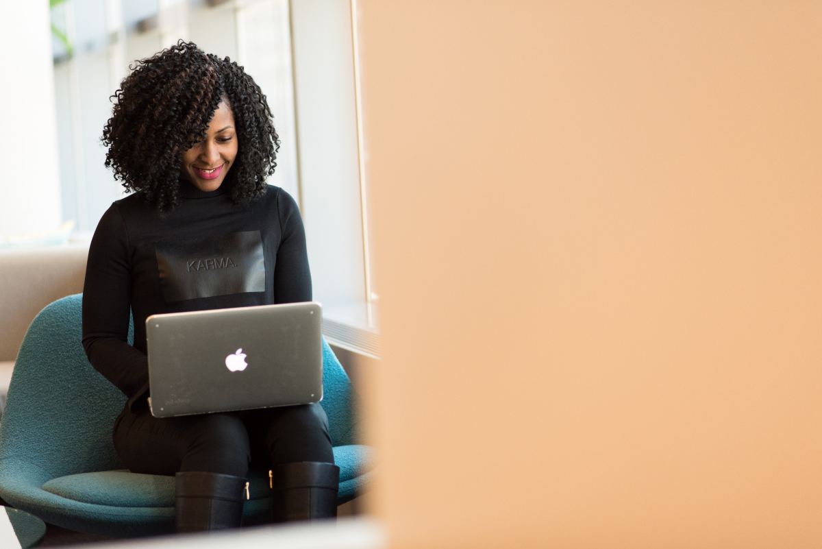 A smiling woman working on her laptop and sitting in a turquoise chair.