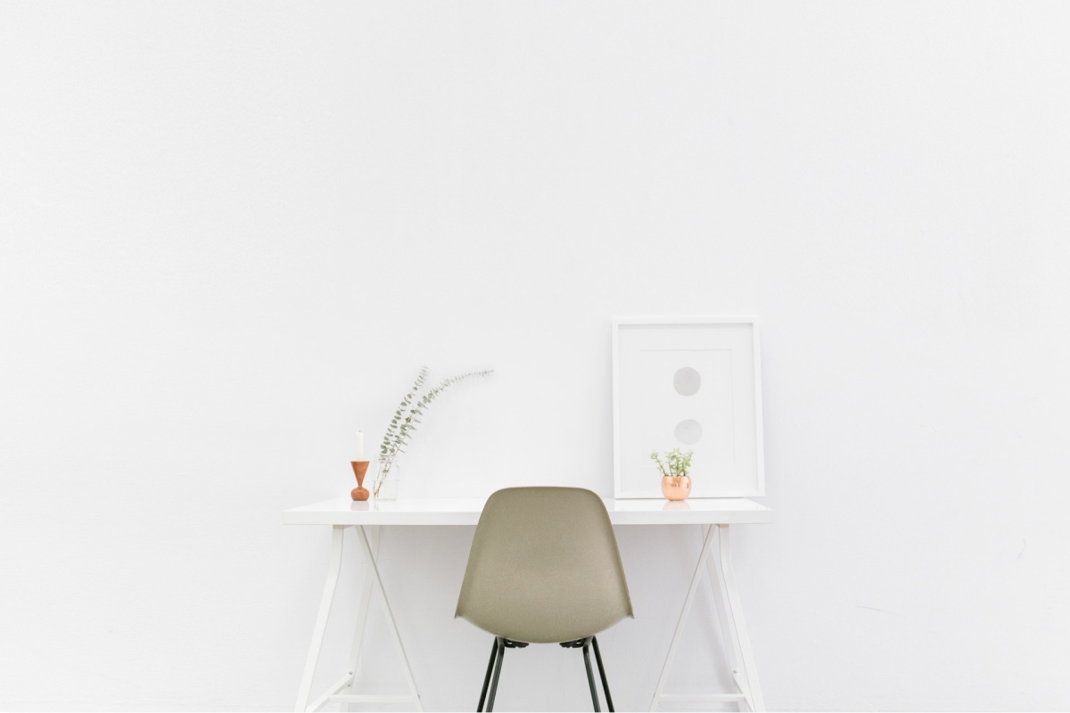 A minimalist desk with a gray chair, two plants, and a piece of art. 
