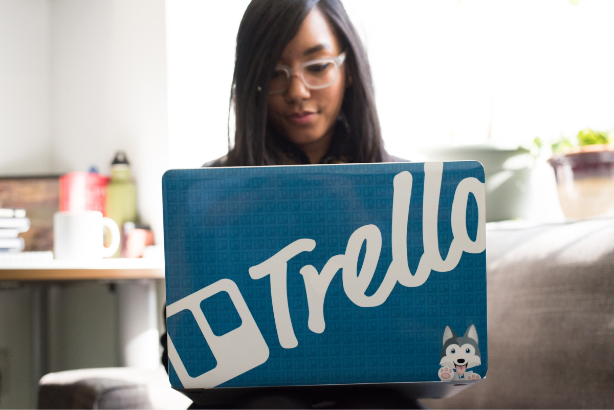 A woman working on a laptop that has a Trello case. 
