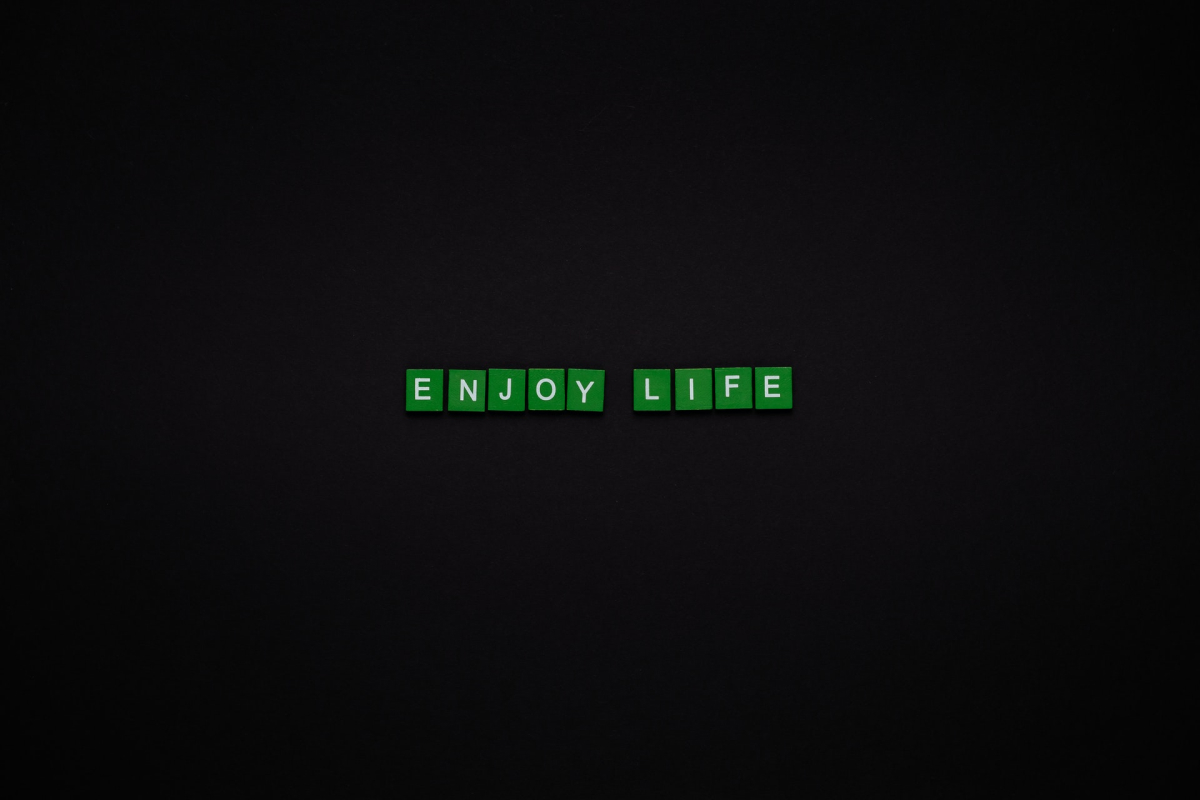 Green tiles with white text on a black background that spell out “enjoy life.”
