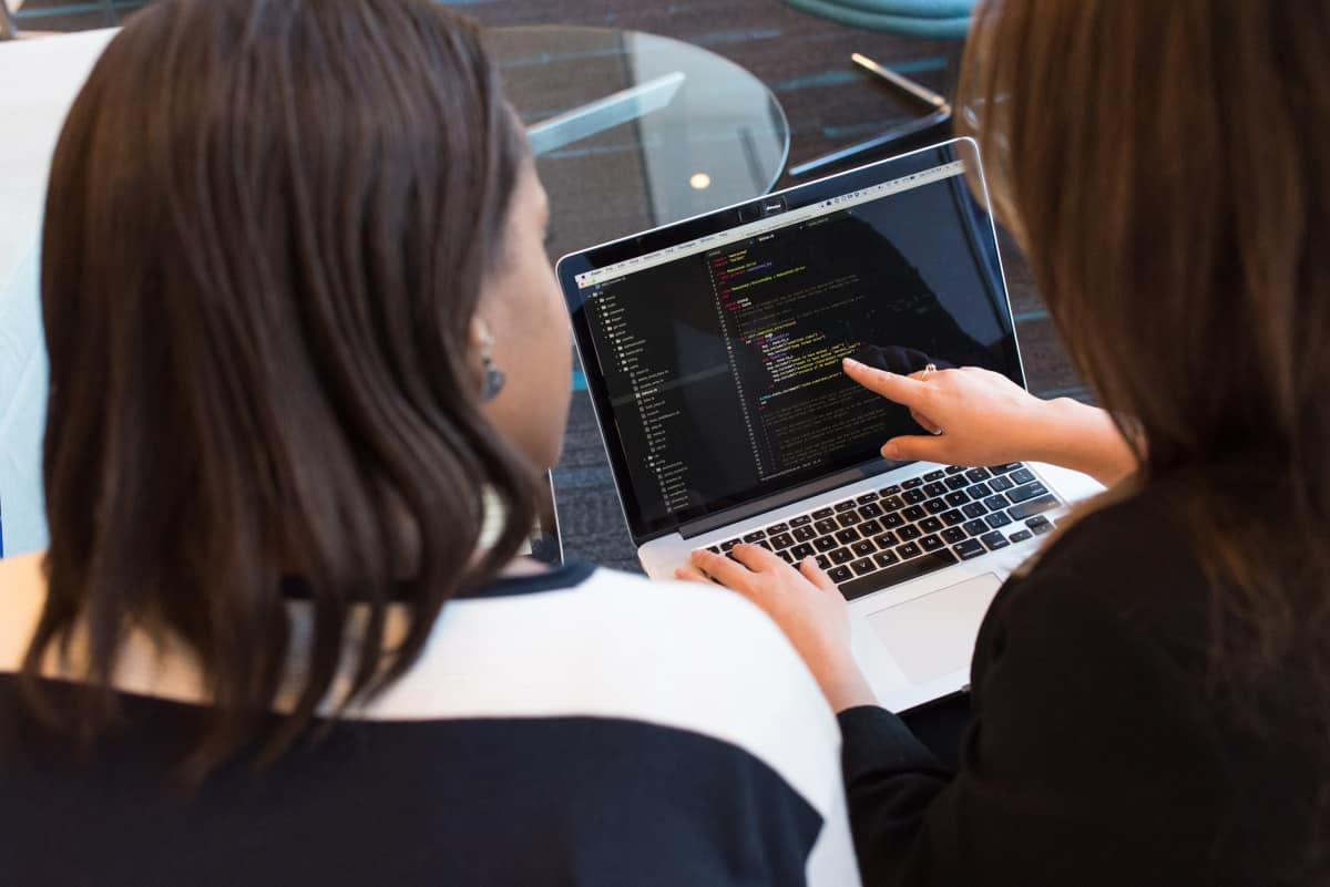 Two women looking at lines of code on a laptop. 